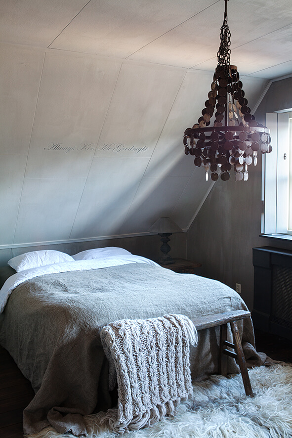 Une chambre d'adulte avec un lit deux places avec des draps gris dans une maison de campagne au style épuré