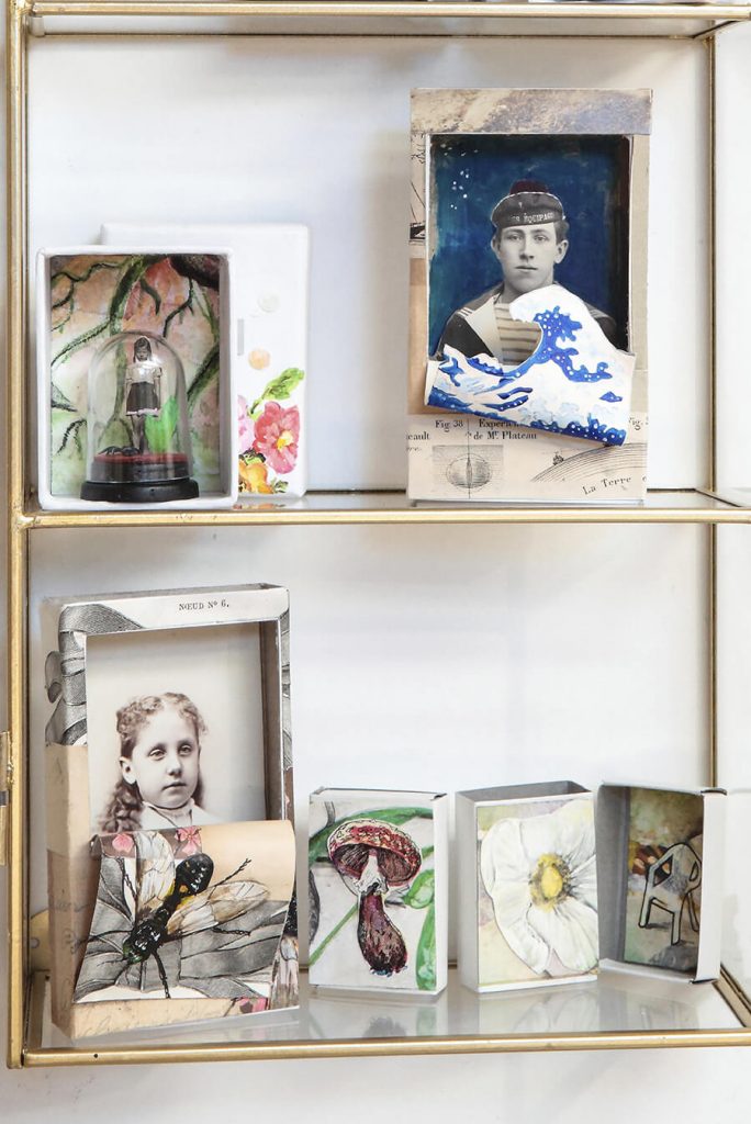 Des dioramas en boite sont exposés dans une vitrine sur deux étagères dont on peut apercevoir des enfants et fleurs