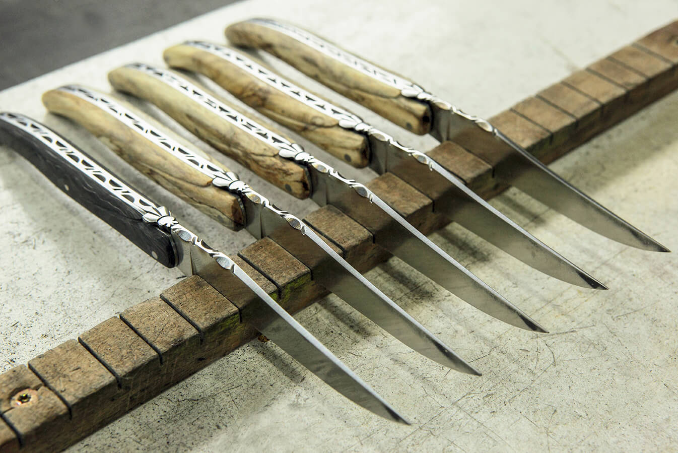 5 couteaux pliants en bois posés sur une planche en bois