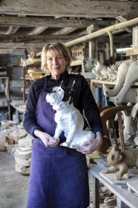 Dominique Kay-Mouat tient dans ses bras un chien en faïence dans son atelier d'épis de faîtage