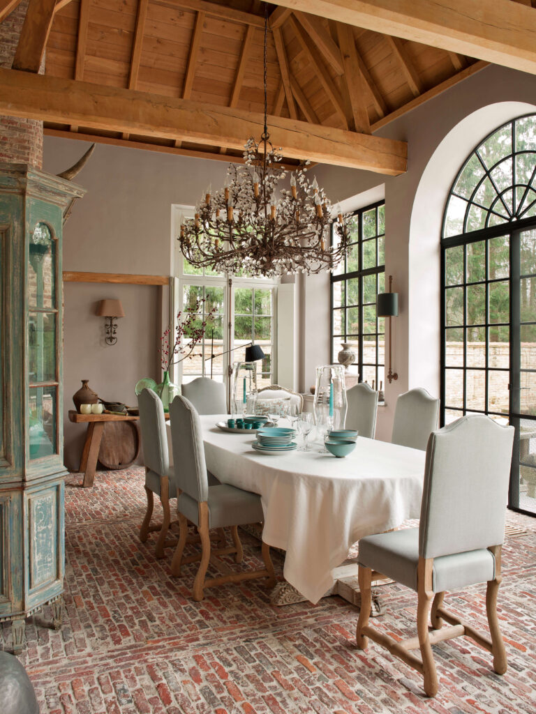 salle à manger avec grand lustre et grande table en bois accompagné de chaises vertes