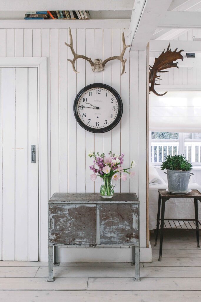 La décoration de la maison mélange les styles rustique, romantique et industriel pour créer une ambiance chaleureuse et accueillante. La petite commode patinée a été dénichée dans une brocante et l’horloge vient de la boutique Pale & Interesting.