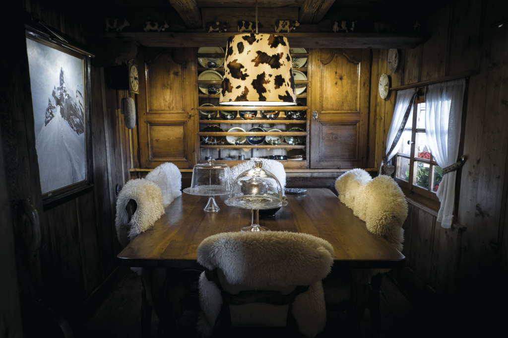 La salle à manger de ce chalet de montagne est décorée dans un esprit montagne avec des peaux de moutons, des tableaux alpins, de la vaisselle ancienne et des figurines de vaches.