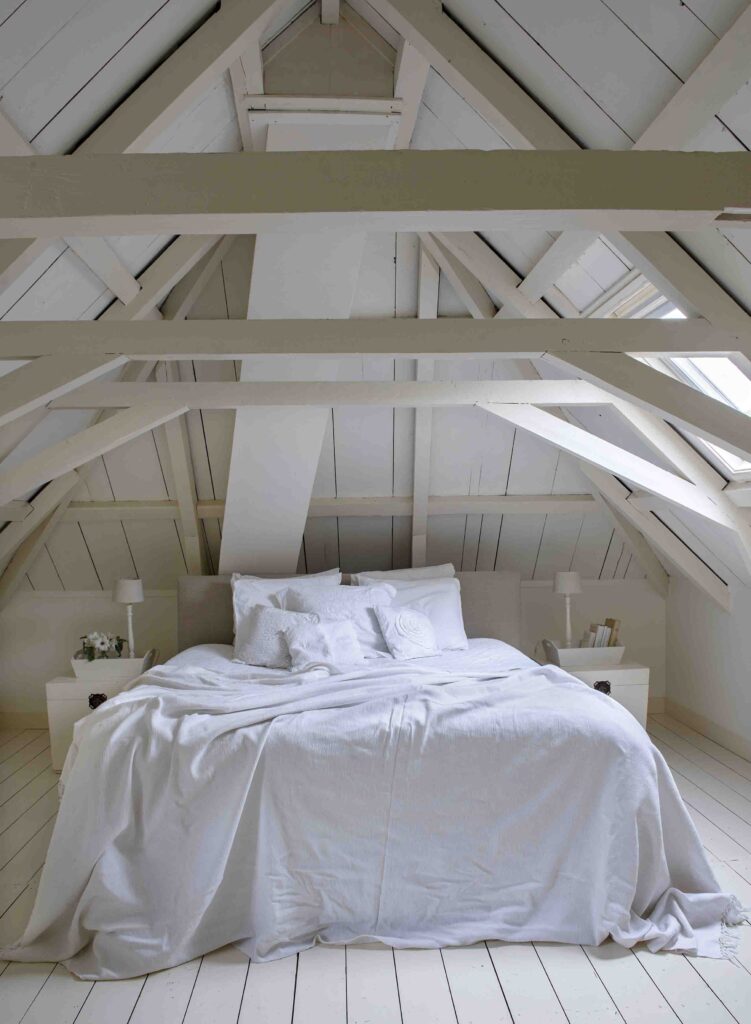 La chambre parentale située sous les combles met parfaitement en avant ces magnifiques poutres en bois peintes en blanc par Mieke.