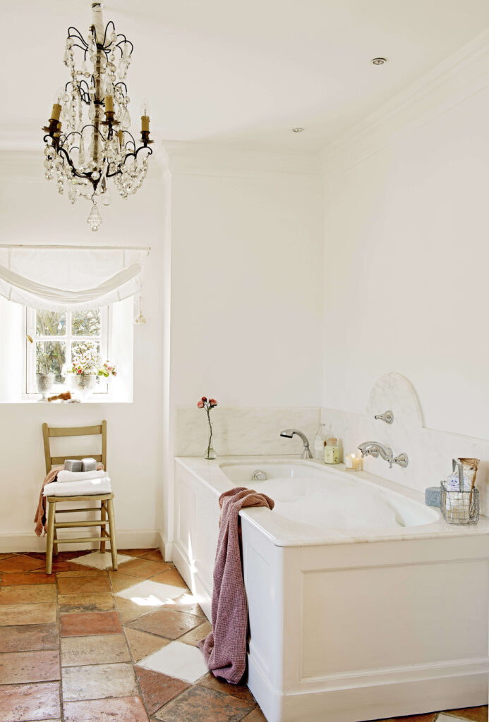 Dans la salle de bains, un meuble provençal en bois blanc accueille le lavabo. la forme arrondie du miroir et les appliques en cristal apportent de l’élégance au lieu.