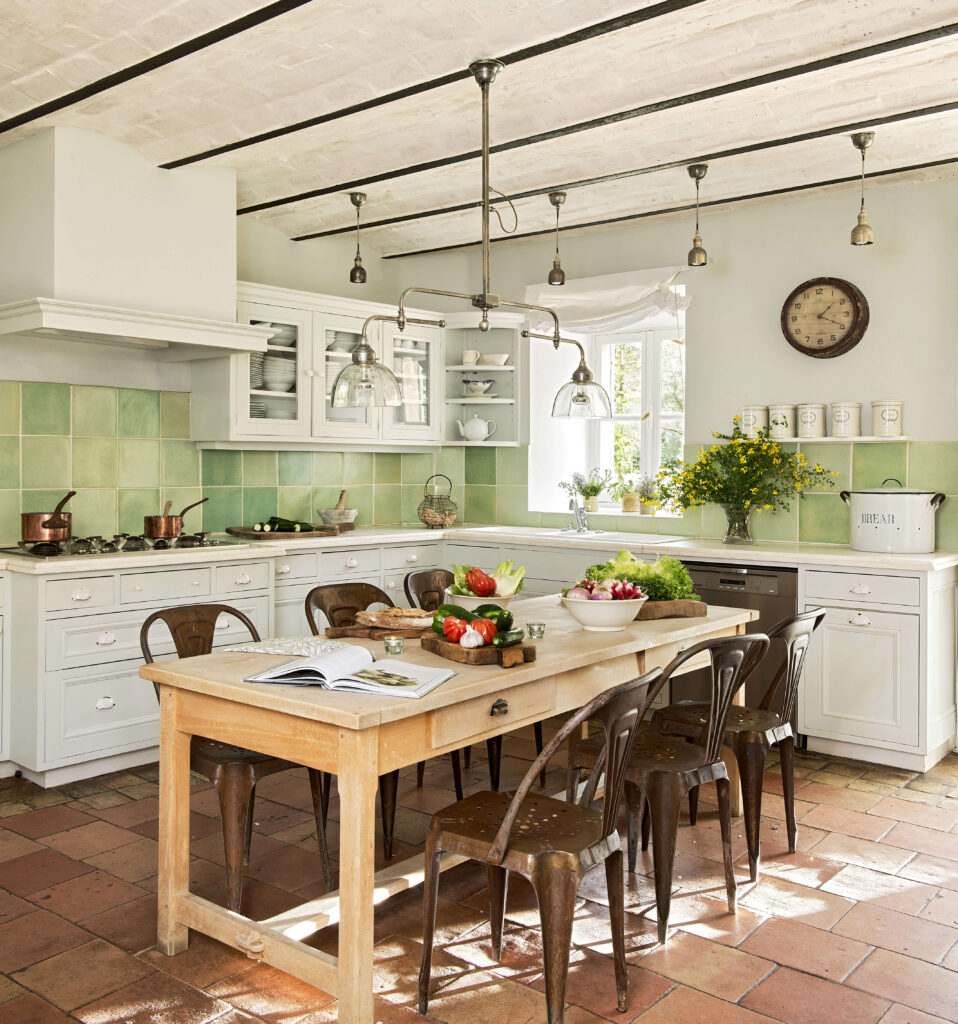 Avec sa cheminée spécialement conçue pour cuisiner, la cuisine provençale arbore un carrelage aux tons verts en parfaite harmonie avec la nature extérieure et des meubles en bois blanc.